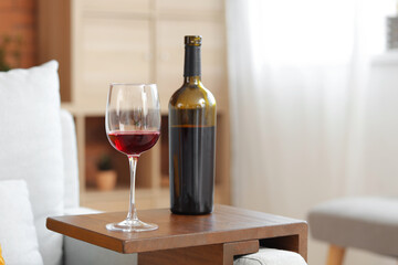 Side table with bottle and glass of red wine in living room, closeup