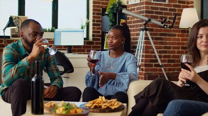 BIPOC friends having entertaining conversation, eating bread sticks from charcuterie board at home. African american, asian and caucasian people throwing party in cozy apartment