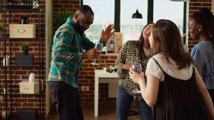 Multiracial mix of guests at home party sharing laughter and dance moves, creating vibrant atmosphere in living room. Friends dancing on hiphop beats during weekend hangout, shaking their hips