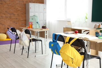 Interior of empty classroom with desks and backpacks on chairs