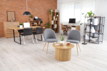 Interior of modern office with workplaces, armchairs and coffee table, blurred view