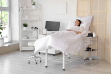 Blurred view of young woman lying on bed in hospital ward