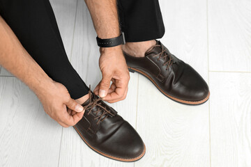 Stylish young businessman tying shoe laces at home, closeup