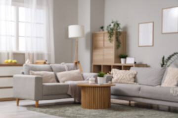Blurred view of of stylish living room with grey sofas, wooden coffee table and houseplants