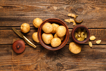 Bowls with raw potatoes and knife on wooden background