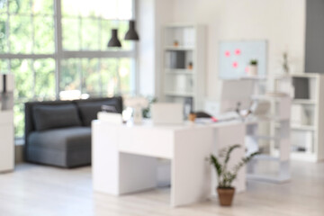 Blurred view of modern office with workplace, couch and shelf units
