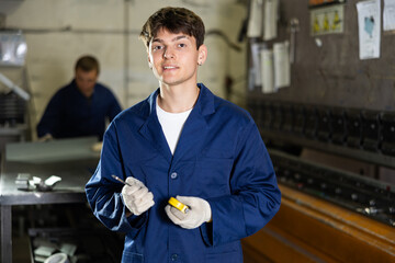 Young male worker in uniform posing with tape measure in metallurgical workshop