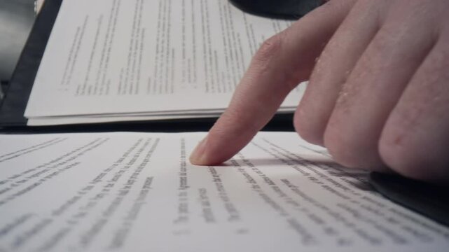Macro shot of hands of unrecognizable businessman opening file with documents and scrolling down with his finger while reading printed text on paper