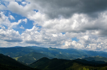 Obraz premium Rolling hills adorned with dense forests. The lush greenery in the foreground contrasts with the layers of mountains in the background, creating a sense of depth under vast sky, dotted with clouds