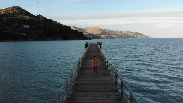woman photographer in colorful clothes enjoys a walk on the Governors Bay Jetty, admiring beautiful coast near Lyttelton and Christchurch in Canterbury, New Zealand South Siland