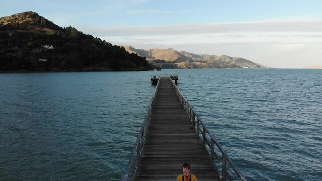 woman photographer in colorful clothes enjoys a walk on the Governors Bay Jetty, admiring beautiful coast near Lyttelton and Christchurch in Canterbury, New Zealand South Siland