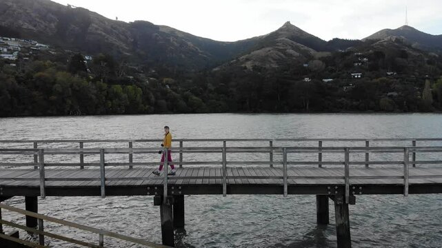 woman photographer in colorful clothes enjoys a walk on the Governors Bay Jetty, admiring beautiful coast near Lyttelton and Christchurch in Canterbury, New Zealand South Siland