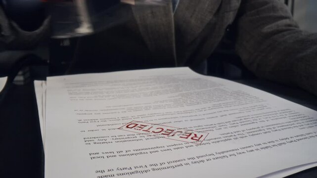 Macro zoom shot of hands of unrecognizable businesswoman sitting at office desk and stamping rejected on document
