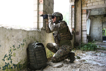 Military mission. Soldier in uniform with binoculars inside abandoned building