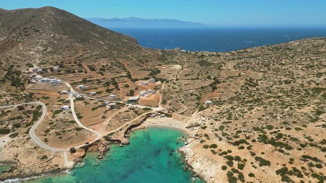 An aerial view of a secluded cove on Donousa island in the Cyclades shows turquoise waters gently lapping at a tranquil crescent-shaped beach