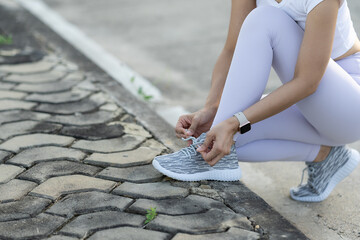 Woman tying shoe laces when jogging in a public park, tying sneakers Concept of people and way of life Health and Wellbeing Theme