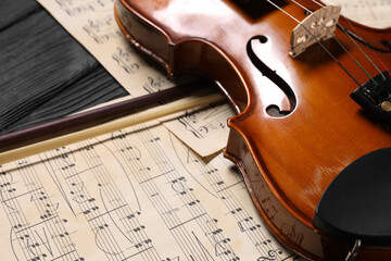 Violin, bow and music sheets on black wooden table, closeup