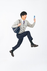 スマホを見ながらジャンプする制服を着た男子学生の全身写真