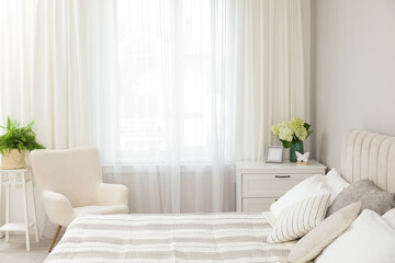 Large bed, chest of drawers, armchair and window with curtains in bedroom. Interior design