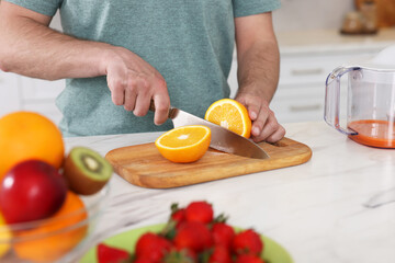 Making juice. Man cutting fresh orange at white marble table in kitchen, closeup