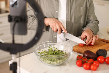 Food blogger cooking while recording video with smartphone and ring lamp in kitchen, closeup