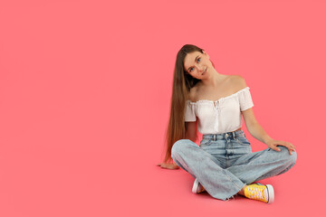 Attractive young girl sits on a pink background