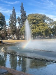 Rainbow appearing over the fountain and reflecting in the water mirror at Plaza Independencia in Mendoza, Argentina, creating a vibrant and picturesque scene