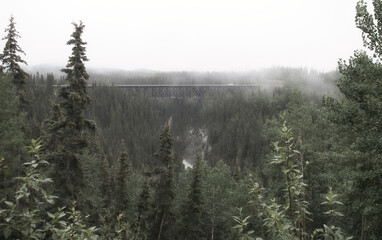 Kuskulana Bridge over gorge with river in Wrangell - St Elias National Park Preserve on a foggy summer day in Alaska.