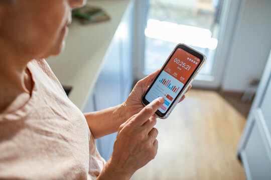 Rear view of a middle aged woman tracking workout time on smartphone