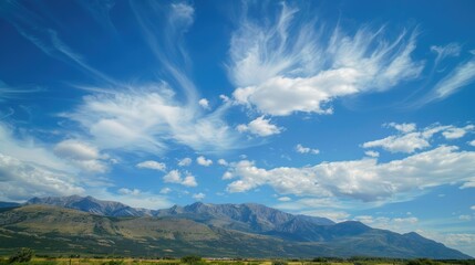 Mountain range under a clear blue sky with soft, white clouds drifting