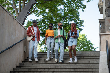 Group of stylish african american friends stroll through city streets, enter underpass, spend time with exciting conversations. Serious black students interested in dialogue communicate walks outside