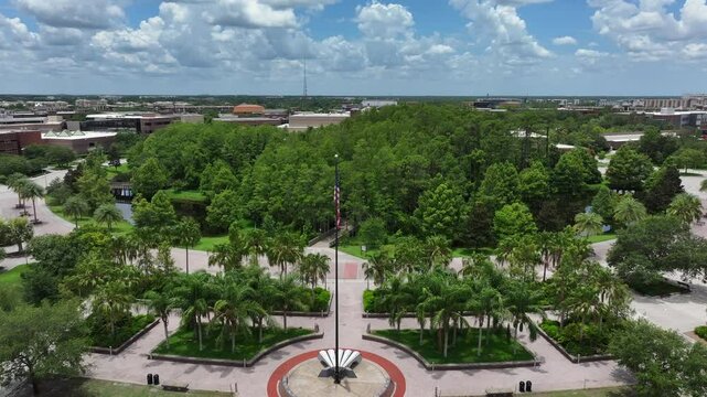 Aerial flyover american flag with green trees between river during sunny day. University of Central Florida, USA.