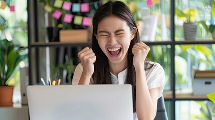 Fototapeta premium Joyful Asian executive in office, excitedly looking at laptop, celebrating good online results