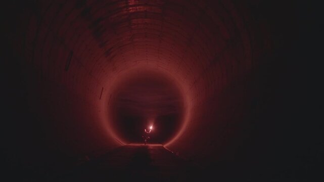 Man running with a red flare through a dark abandoned subway tunnel made of reinforced concrete (ProRes 422HQ, 4K)