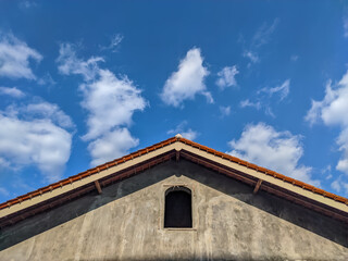 A house roof with a skylight framed by a backdrop of blue sky and fluffy clouds offers a stunning visual treat.