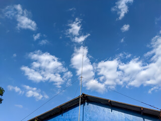 Fototapeta premium An FM transceiver antenna perched on a rooftop against a backdrop of blue sky and scattered clouds captures a scene of modern connectivity.