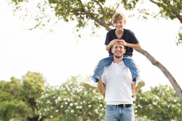 Man piggyback his son on a shoulder and walking around the park.