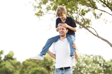 Man piggyback his son on a shoulder and walking around the park.