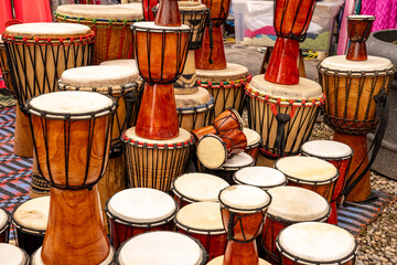 Traditional handmade djembe drums displayed at a market. The single-headed goblet drum comes from...