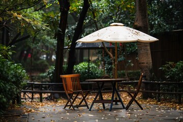 Obraz premium Wooden table and chairs standing on wet ground under white umbrella in park during rainy autumn day