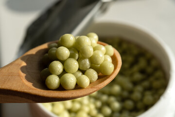 Selective focus on wooden spoon with small green round homeopathic pills on open jar background.
