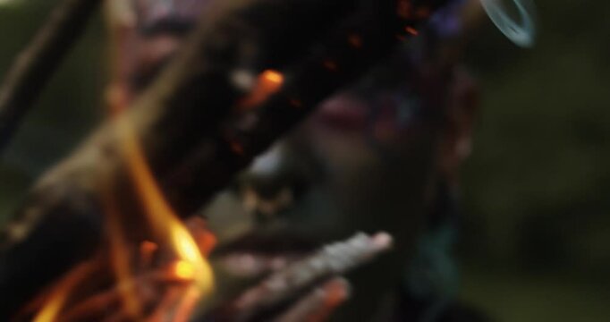 Closeup of a fire Mystical performer in tribal face paint, holding a flaming burning stick. Capturing intense emotions and ancient rituals in a dark outdoor scene with a mysterious vibe.