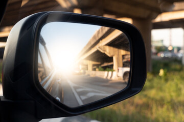 Naklejka premium Mirror view from the side of the car can see the bridge and the road. Light shot straight into the middle of the asphalt road.