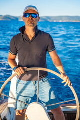 Young man captain stands at the helm and controls a sailboat during a journey by sea