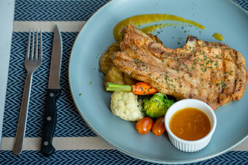 Pork steak and vegetables on a blue plate There was a sparring racket and a knife next to it.