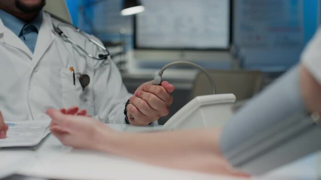 Cropped pan shot of unrecognizable general practitioner in scrubs and with stethoscope over neck taking patients blood pressure squeezing sphygmomanometer bulb during annual checkup in state hospital