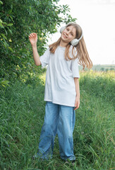 A child  with headphones listening to music and dancing in the park.