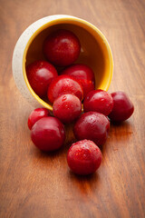 Front view of fresh Cherry Plum (Prunus cerasifera) fruits spilled out from a ceramic bowl on a wooden background.