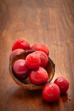 Front view of fresh Cherry Plum (Prunus cerasifera) fruits in a coconut shell on a wooden background.