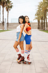 Portrait of two friends, back-to-back with roller skates, both smiling and enjoying their time together in an urban park.